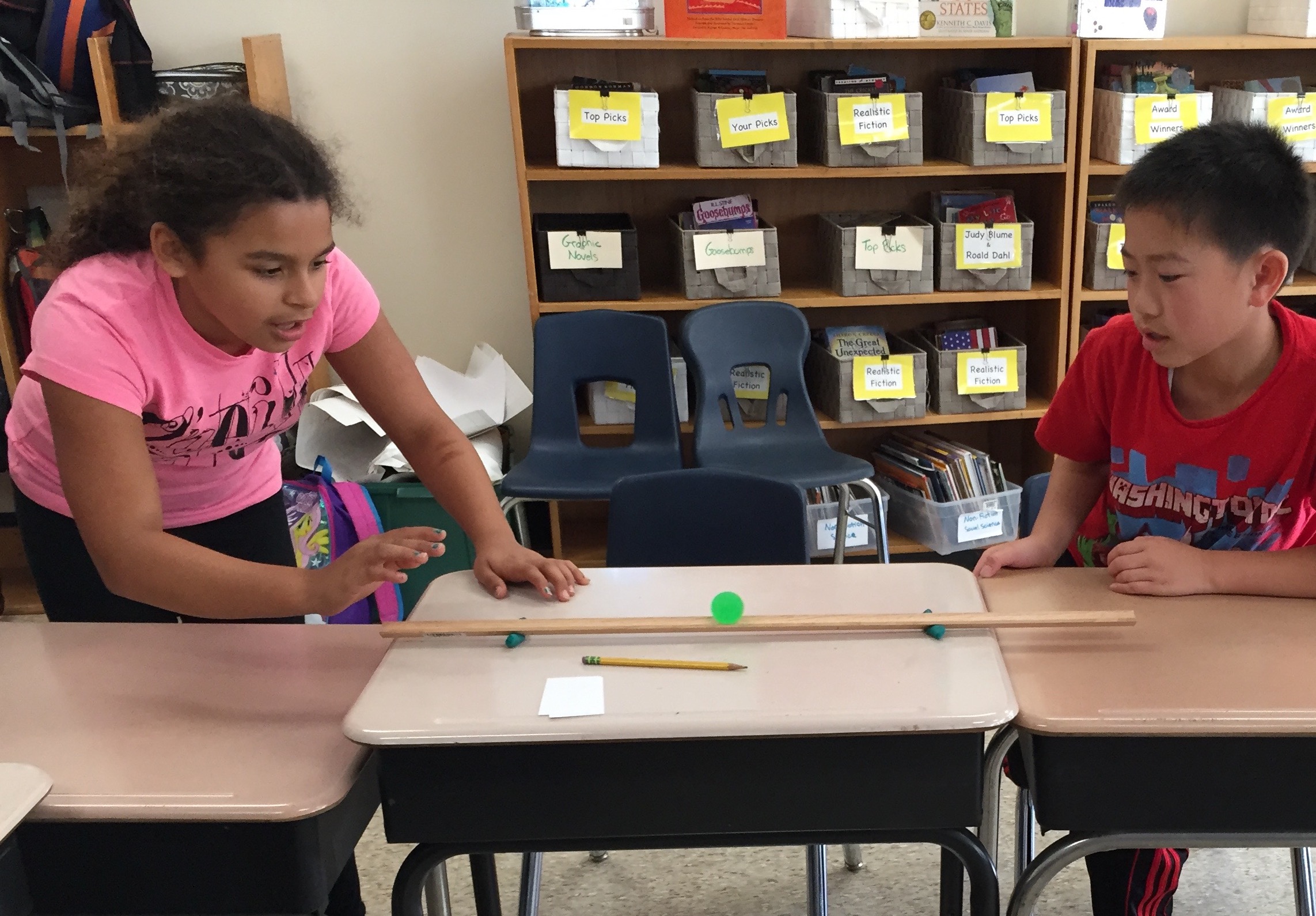 Two students watch a ball on a track.